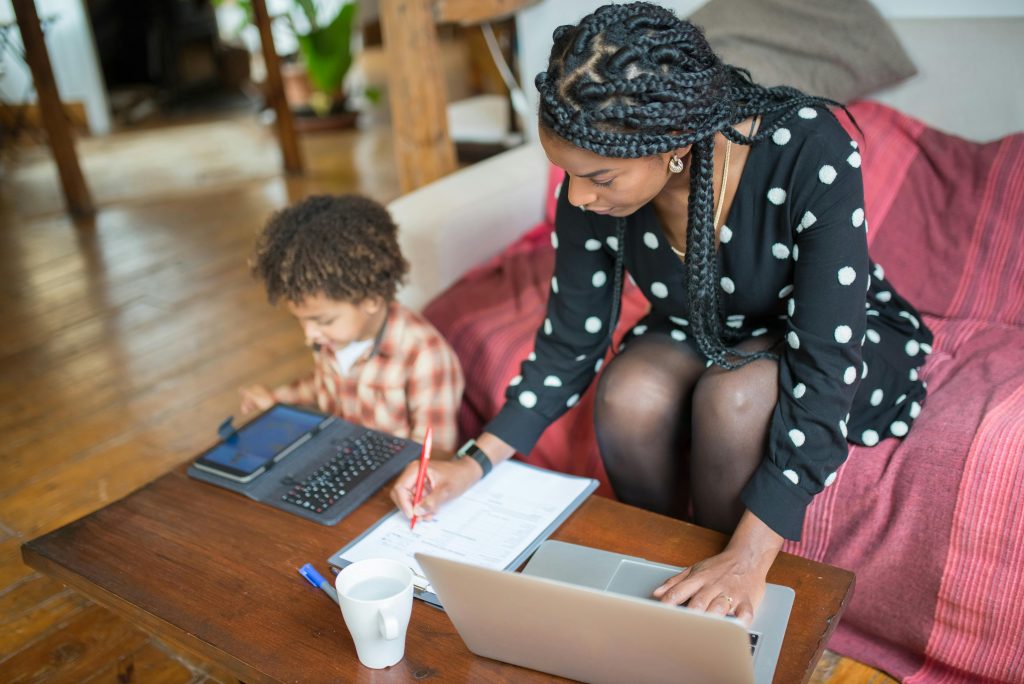 A parent and child learning together at home using a laptop and tablet.