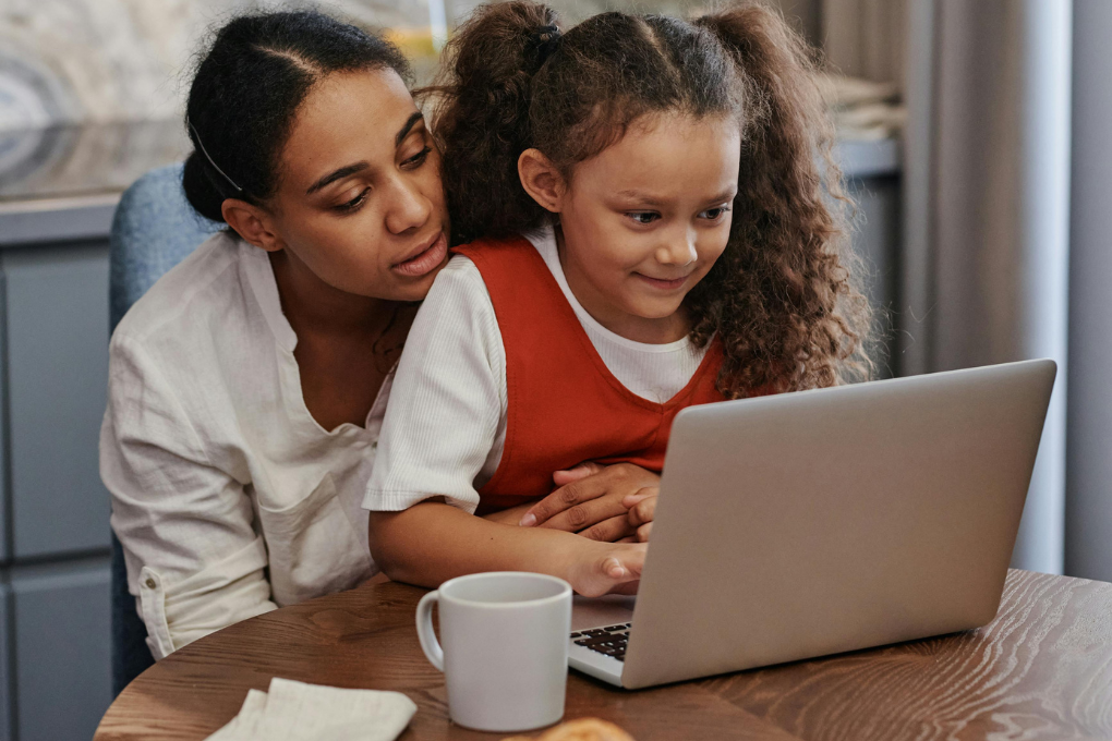 Mother and daughter using a laptop together at the kitchen table