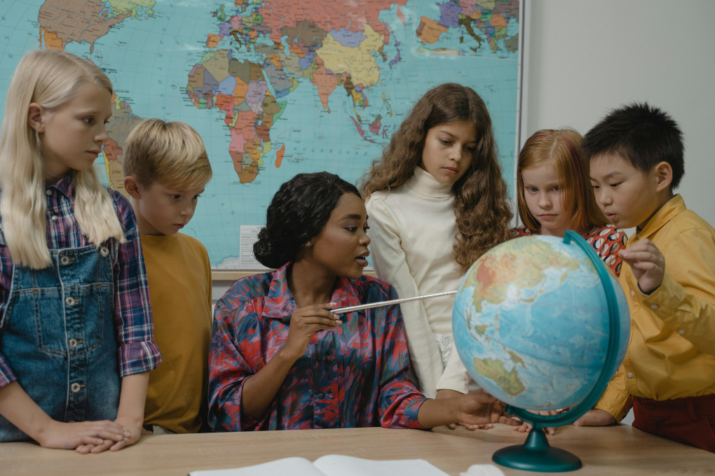 Teacher using a globe to teach geography to a group of young students